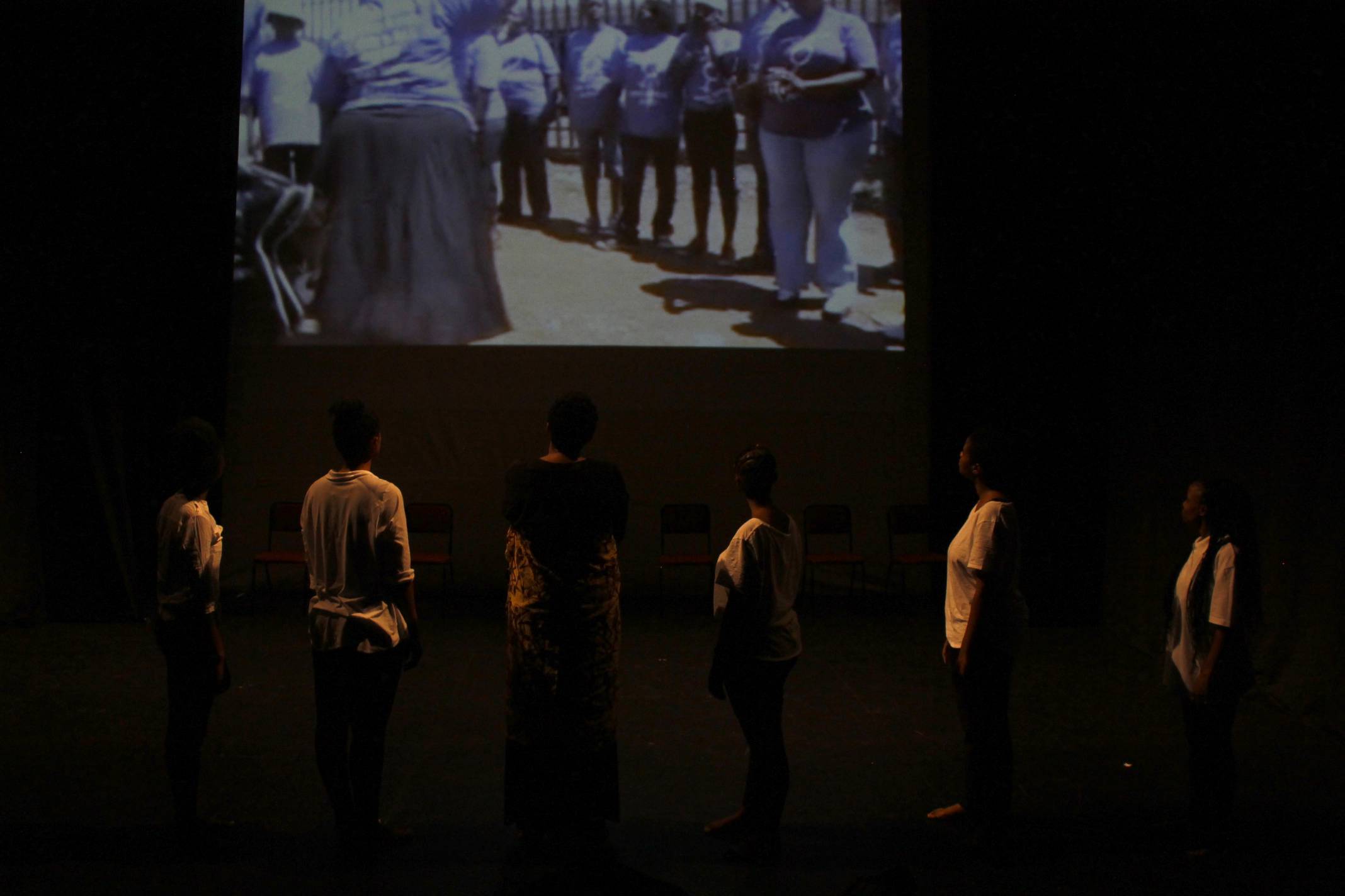 The performers watch research footage. <br>Photo Credit: (c) Madoda Mkhobeni